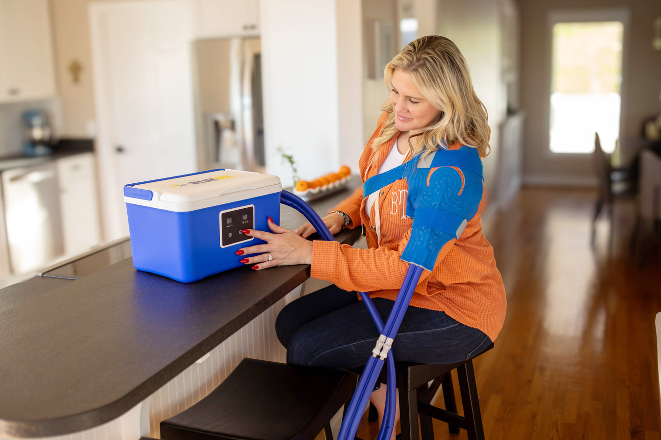 Brittany Jackson using a Brace Direct blue ice therapy machine while seated at a kitchen counter