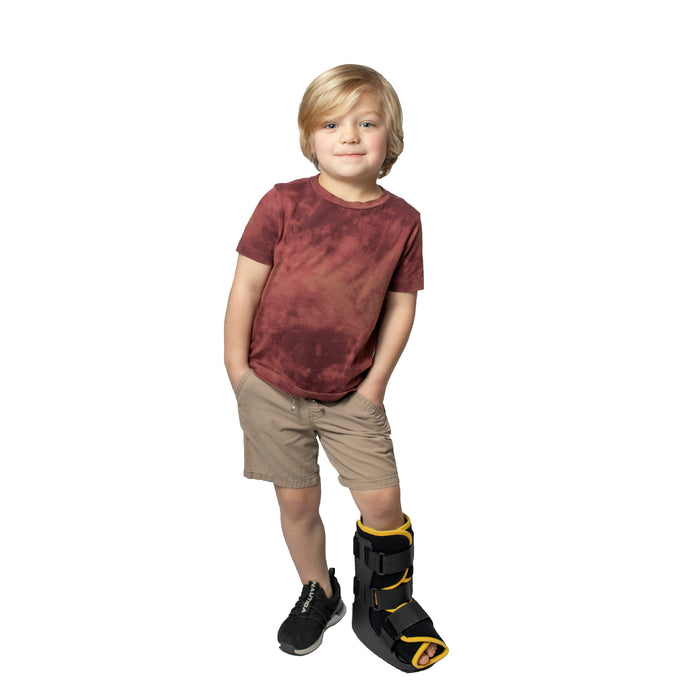 A smiling boy demonstrates the fit of the yellow Brace Direct Pediatric Walker Fracture Boot.