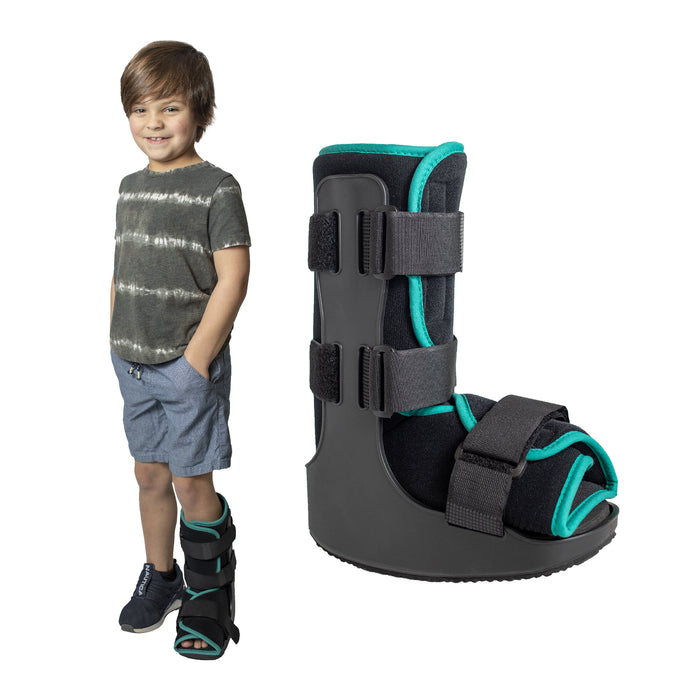 A smiling boy demonstrates the fit of the green Brace Direct Pediatric Walker Fracture Boot, beside a side view of the boot in green.